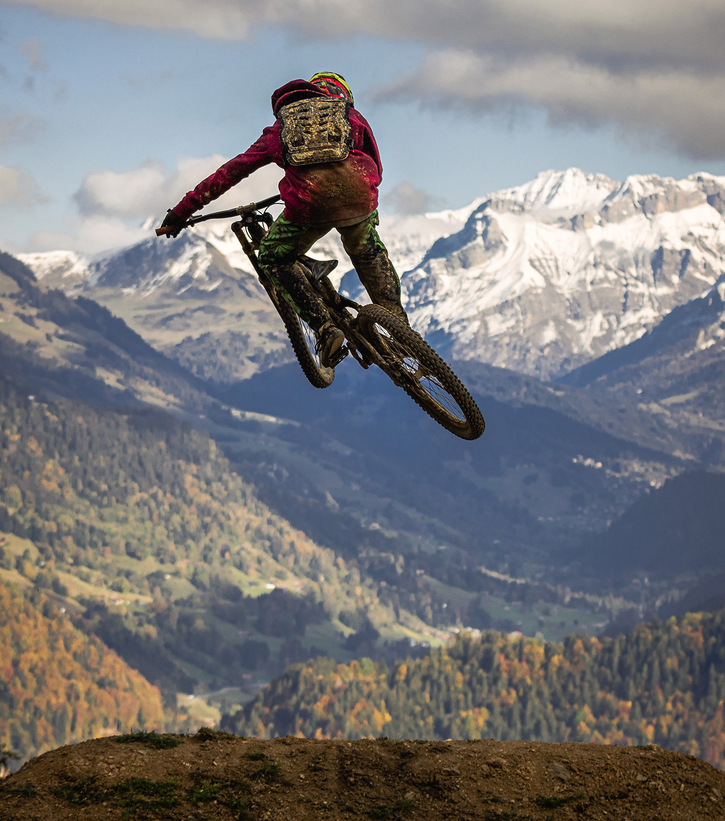 Veduta posteriore di una persona in abbigliamento sportivo che salta con una mountain bike. Paesaggio alpino innevato sullo sfondo.