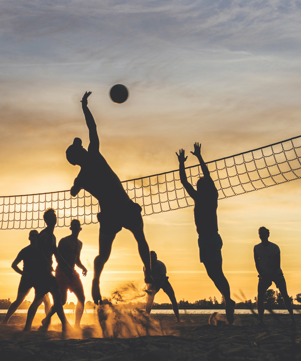 Sagome di persone che giocano a beach volley al tramonto.