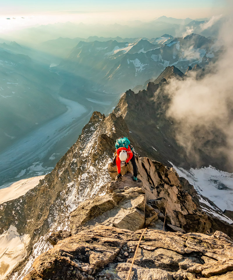 Persona in abbigliamento da alpinismo sulla cresta di una montagna innevata.